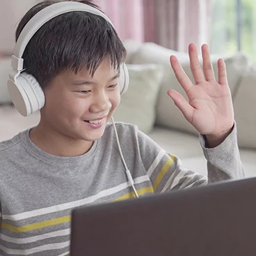 student wearing headphones and waving at computer screen