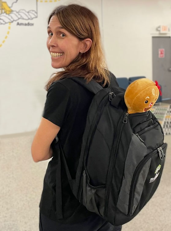 female teacher wearing backpack with stuffed gingerbread toy in the pocket