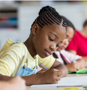 African American girl in yellow shirt leaning over a desk and writing on a piece of paper
