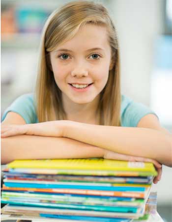 girl with long blonde  hair sitting with arms folded across each other in front of her and resting on a stack of books