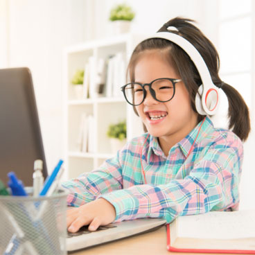Young Asian girl with glasses wearing headphones and using a laptop computer on a desk