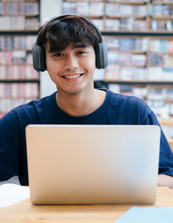 high school student sitting behind laptop computer smiling and wearing headphones