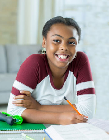 African American girl leaning on her elbows on a desk with a book in front of her and smiling at the camera